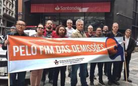 Imagem mostra dirigentes do Sindicato dos Bancários de São Paulo em frente ao Quarteirão de Investimentos, portando uma faixa onde se lê "pelo fim das demissões"