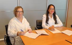 Imagem mostra Wanessa de Queiroz, coordenadora da Comissão de Organização dos Trabalhadores do Santander e uma representante do Santander, sentadas lado a lado, em frente a uma mesa, em uma sala, assinando o acordo de compensação de horas negativo
