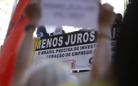 Imagem de ato pela redução de juros, focado em um cartaz onde se lê "menos juros"