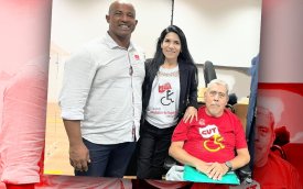 Fotografia mostra integrantes do Conade: Um homem negro camisa branca, mulher ao meio de cabelos pretos e um homem sentado na cadeira de rodas 
