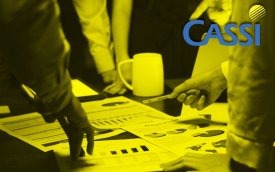 Imagem mostra pessoas debruçadas sobre uma mesa com vários papeis sobre ela. No canto superior direito está posicionado o logo da Cassi. A imagem tem um filtro amarelo 