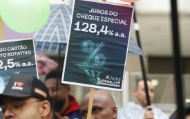 Imagem mostra um homem segurando um cartaz onde ser lê Juros do cheque especial 128,4% a.a.#JurosBaixosJá, durante atop das centrais sindicais pela redução dos juros