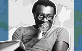 Imagem de Milton Santos, um homem negro, de óculos, sorrindo, na faixa dos 50 a 60 anos.