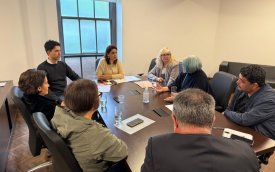 Imagem mostra reunião entre representantes do INSS e do Sindicato dos Bancários. São oito pessoas - cinco mulheres e três homens em volta de uma mesa oval marrom, em uma sala de parede branca