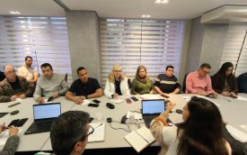 Imagem mostra representantes dos trabalhadores reunidos com representantes do banco, dentro de uma sela e sentados frente a frente em um mesa branca e comprida