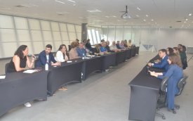Imagem mostra sala onde ocorreu a reunião para discutir o Saúde Caixa. a imagem mostra 12 pessoas sentadas lado a lado em uma mesa comprida. Atrás dela há uma janela que ocupa toda a parede. 