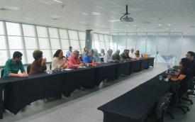 Imagem mostra sala onde ocorreu a reunião para discutir o Saúde Caixa. a imagem mostra 12 pessoas sentadas lado a lado em uma mesa comprida. Atrás dela há uma janela que ocupa toda a parede. 