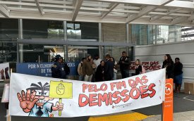 Imagem mostra protesto em frente a uma agência do Itaú, com uma faixa exposta em primeiro plano onde se lê "pelo fim das demissões"