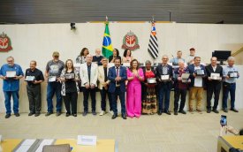 Imagem mostra personagens que fizeram a greve de 1985. Eles estão lado a lado na sala da assembleia legislativa de são paulo e seguram placas de homenagem