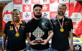 fotografia mostra 3 homens brancos cegos, com camisa preta, um deles boné e medalha de participação no peito
