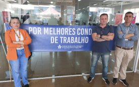 Imagem mostra dirigentes sindicais na porta de uma agência e ao lado de uma faixa onde se lê "por melhores condições de trabalho"