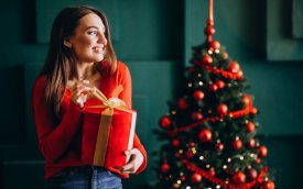 Imagem de uma mulher segurando um presente, com árvore de natal ao fundo