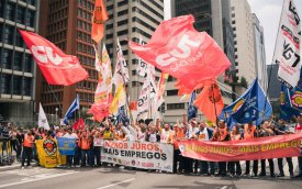 Imagem mostra manifestantes portando bandeiras da CUT durante atividade pela redução dos juros