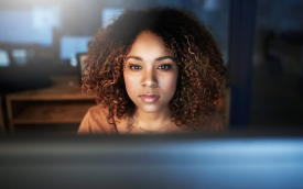 Mulher negra e jovem em frente a um computador e com semblante sério