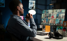 Imagem mostra um jovem negro em frente a um computador que projeta rostos de outras pessoas, com se fosse uma reunião virtual