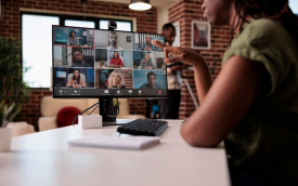 imagem mostra uma pessoa negra em frente a um computador em cuja tela estão projetados os rostos de várias pessoas, simulando uma reunião virtual