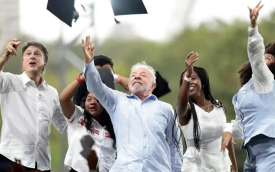 Imagem mostra Lula ao lado de esatudantes enquanto jogam capelos para cima