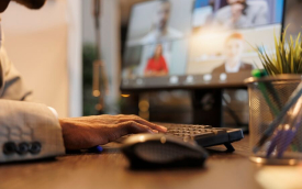 Imagem mostra um homem em frente a um computador, participando de uma reunião remota. a tela do computador exibe os rostos de outros participantes da reunião