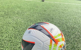 Campo de futebol com uma bola Penalty Mag11a F2 centralizada. Ao fundo as dependências do estádio Nicolau Alayon.