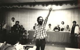 Foto de Augusto Campos, com o braço erguido