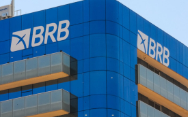 Imagem mostra o alto da fachada do prédio do BRB. o edifício é espelhado com vidros azuis. a imagem foca no lato da fachada, que exibe o logo do banco