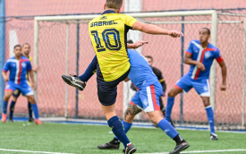 Jogador vestindo a camiseta do Equador chutando uma bola contra 3 adversários de azul