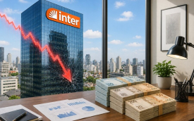 Imagem mostra uma pillha de dinheiro sobre uma mesa em uma sala com uma janela com vista para um prédio com um letreiro do Banco Inter. sobre o prédio há um gráfico em linha na cor vermelha indicando queda