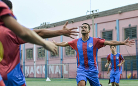 Jogador de futebol após marcar um gol correndo para receber o abraço dos companheiros.