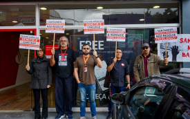imagem mostra dirigentes perfiladas portando placas em frente a uma agência do Santander durante protesto 