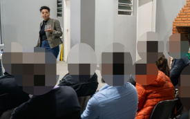 Imagem mostra a dirigente susana malu córdoba falando a bancários durante plenária. Ela está em pé em, um tablado, em frente aos bancários, que estão sentados. Susana é uma mulher negra, de cabelos curtos na faixa dos 35 anos