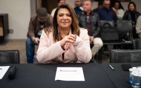 Neiva Ribeiro, presidenta do Sindicato dos Bancários, veste um blazer branco e usa óculos. Está sentada, com os braços apoiados em uma mesa, e dedos das mãos entrelaçados, na altura do peito