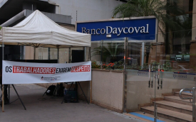Imagem mostra faixa escrita "os trabalhadores exigem respeito" estendida em frente ao prédio do Daycoval e ao lado de uma placa com o logo do banco