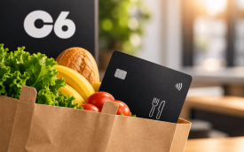 Imagem feita por inteligência artificial composta por um cartão de vale-alimentação na cor preta dentro de um sacola de papel junto com frutas e legumes. ao fundo o logo do C6