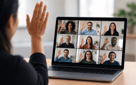 imagem mostra mulher com a mão levantada em frente a uma tela de computador em cuja tela são projetadas diversos rostos de pessoas em uma reunião virtual 