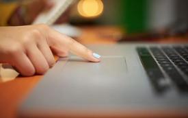 Imagem mostra computador do tipo laptop sendo manuseado por uma mão feminina de pele branca