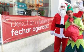 Atores fantasiados de Papai Noel e de duende ao lado de uma faixa colocada em frente à uma agência do Bradesco, com o dizer: "Desafiar o futuro é fechar agências?" 