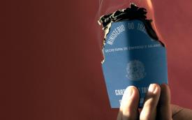 Imagem mostra mão masculina segurando uma carteira de trabalho em chamas, sob um fundo vermelho