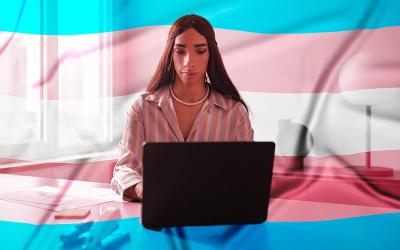 Imagem de uma mulher trans sentada em frente a um computador. Ao fundo, um filtro com a bandeira da visibilidade trans