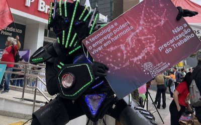 Fotografia de um robô, segurando uma placa que diz que o emprego e a tecnologia podem conviver em harmonia, durante ato da Campanha dos Bancários 2024 na Faria Lima