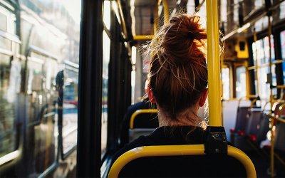 Imagem mostra uma mulher de costas, sentada em um banco dentro de um ônibus