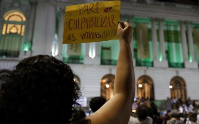 Mulher segura um carta escrito "para de culpabilizar as vítimas"