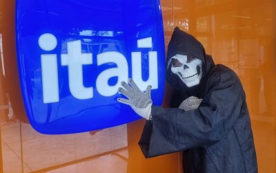 Imagem mostra uma pessoa vestida de morte ao lado do logo do Itaú que ostenta uma agência palco de protesto por demissões