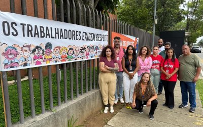 Imagem mostra grupo de dirigentes sindicais durante protesto do Sindicato contra o banco Pan. Eles estão na frente da fachada do prédio do banco, em frente a uma faixa onde se lê "os trabalhadores exigem respeito"