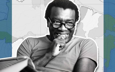 Imagem de Milton Santos, um homem negro, de óculos, sorrindo, na faixa dos 50 a 60 anos.