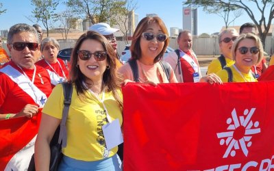 Fotografia mostra mulheres, uma de blusa vermelho e outra de amarela, segurando faixa vermelha