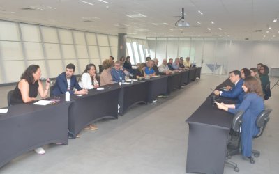 Imagem mostra sala onde ocorreu a reunião para discutir o Saúde Caixa. a imagem mostra 12 pessoas sentadas lado a lado em uma mesa comprida. Atrás dela há uma janela que ocupa toda a parede.