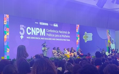 Imagem mostra plenário da 5ª conferencia nacional de política para as mulheres. a imagem foca o palco do evento enquanto discursa Sonia Guajajara, Ministra dos Povos Indígenas do Brasil