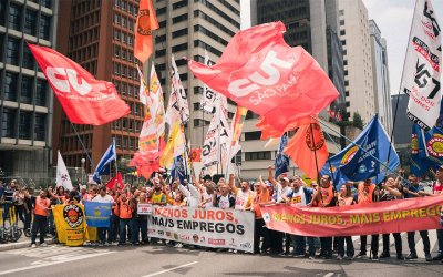 Imagem mostra manifestantes portando bandeiras da CUT durante atividade pela redução dos juros