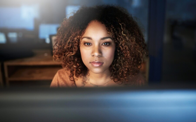 Mulher negra e jovem em frente a um computador e com semblante sério