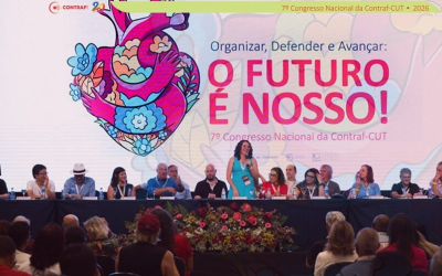 Imagem mostra dirigentes lado a lado no palco do 7º Congresso Nacional da Contraf-CUT. Atrás deles há um telão imenso com uma arte formada por um coração estilizado ao lado do texto "O Futuro é Nosso"